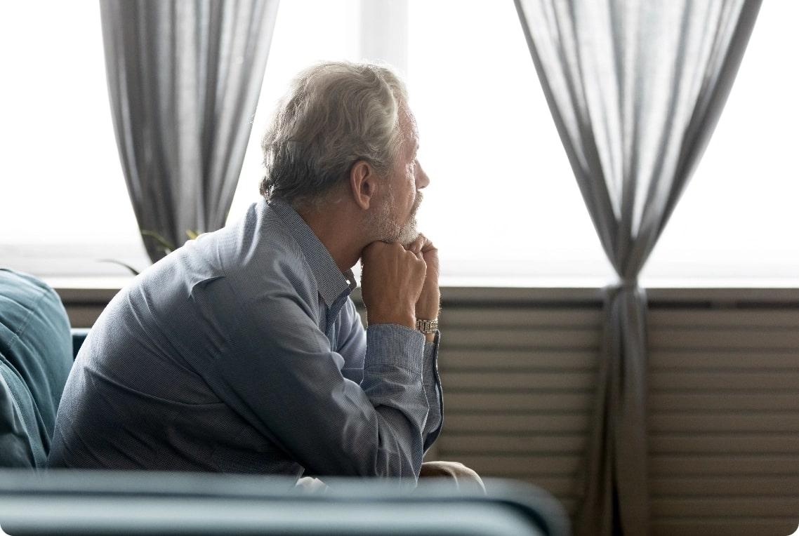 Un homme âgé qui regarde par la fenêtre.